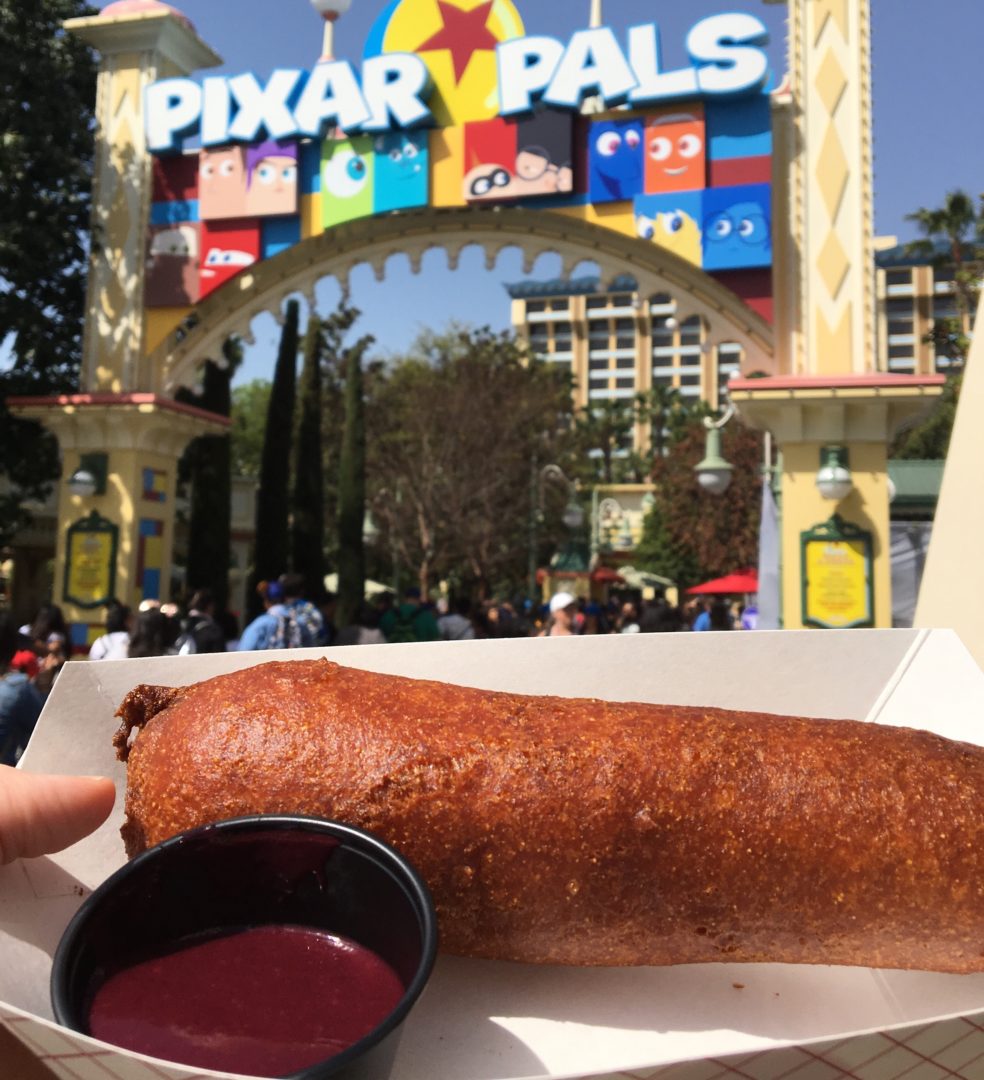 Three-Flavored Spicy Corn Dog with Blackberry Serrano Dipping Sauce in front of Pixar Pals Sign at Disneyland